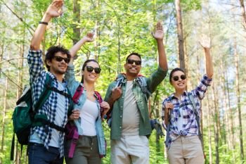 travel, tourism, hike and people concept - group of friends with backpacks waving hands in forest. group of friends with backpacks hiking in forest