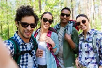travel, tourism, hike and people concept - group of friends with backpacks taking selfie in forest. friends with backpacks hiking and taking selfie