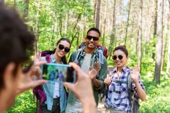 travel, tourism and hike concept - group of friends with backpacks being photographed by smartphone in forest. friends with backpacks being photographed on hike