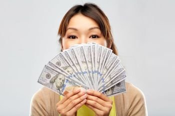 people, ethnicity and portrait concept - happy asian young woman holding hundreds of dollar money banknotes over grey background. asian woman with hundreds of dollar money