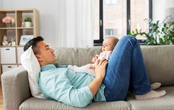 family, parenthood and fatherhood concept - happy middle aged father with little baby daughter lying on sofa at home. middle aged father with baby lying on sofa at home