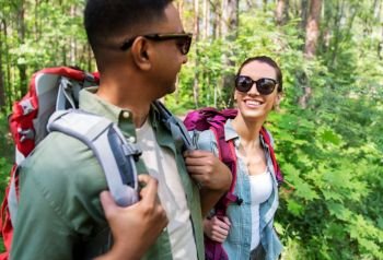 travel, tourism, hike and people concept - mixed race couple walking with backpacks in forest. mixed race couple with backpacks hiking in forest