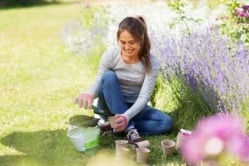 gardening and people concept - happy young woman filling pots with soil at summer garden. woman filling pots with soil at summer garden
