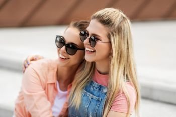leisure and friendship concept - happy smiling teenage girls or best friends in sunglasses hugging on city street in summer. teenage girls or friends on city street in summer