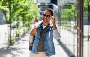 travel, tourism and lifestyle concept - smiling indian man in sunglasses with backpack on city street. indian man in sunglasses with backpack in city
