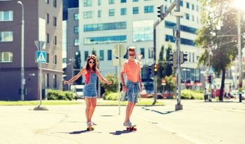 summer holidays, extreme sport and people concept - happy teenage couple riding short modern cruiser skateboards on city street. teenage couple riding skateboards on city street