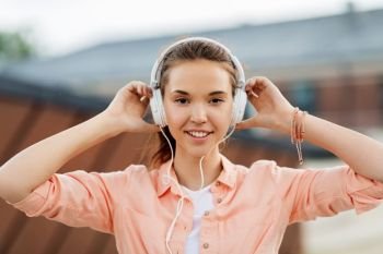 music, summer and leisure concept - happy teenage girl with headphones in city. happy teenage girl with headphones in city