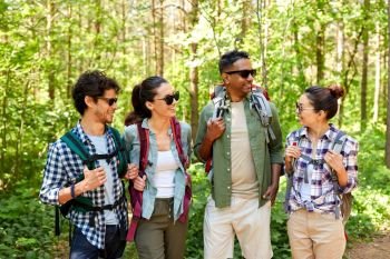 travel, tourism, hike and people concept - group of friends with backpacks talking in forest. friends with backpacks on hike talking in forest