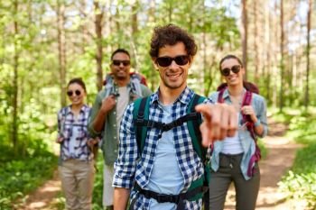 travel, tourism, hike and people concept - group of friends with backpacks and man pointing finger to you in forest. friends with backpacks on hike in forest