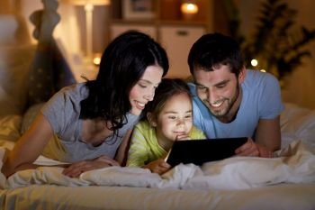 people and family concept - happy mother, father and little daughter with tablet pc computer in bed at night at home. family with tablet pc in bed at night at home