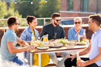 leisure and people concept - happy friends having dinner or bbq party on rooftop in summer. friends having dinner or bbq party on rooftop