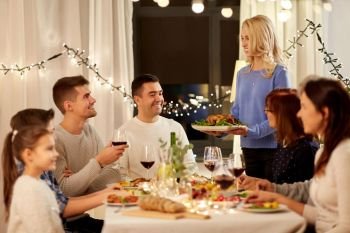 celebration, holidays and people concept - happy woman offering roast chicken to family having dinner party at home. happy family having dinner party at home