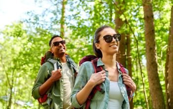 travel, tourism, hike and people concept - mixed race couple walking with backpacks in forest. mixed race couple with backpacks hiking in forest