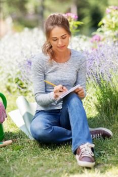 gardening and people concept - young woman writing to notebook at summer garden. young woman writing to notebook at summer garden