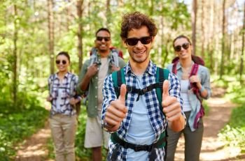 travel, tourism, hike and people concept - group of friends with backpacks and man showing thumbs up gesture in forest. friends with backpacks showing thumbs up in forest