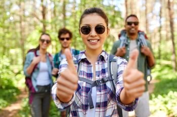 travel, tourism, hike and people concept - group of friends with backpacks and asian woman showing thumbs up gesture in forest. friends with backpacks showing thumbs up in forest