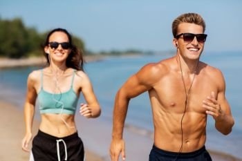 fitness, sport and technology concept - happy couple with earphones running along summer beach. couple with earphones running along on beach