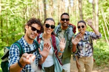travel, tourism, hike and people concept - group of friends with backpacks taking picture by selfie stick and waving hands in forest. friends with backpacks hiking and taking selfie