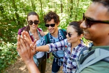 travel, tourism, hike and people concept - group of friends with backpacks talking and making high five in forest. friends with backpacks hiking and making high five
