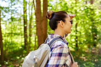 travel, tourism, hike and people concept - happy asian woman with backpack looking far away in forest. happy asian woman with backpack hiking in forest