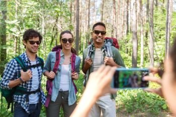 travel, tourism and hike concept - group of friends with backpacks being photographed by smartphone in forest. friends with backpacks being photographed on hike