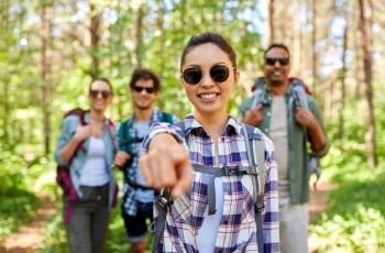 travel, tourism, hike and people concept - group of friends with backpacks and asian woman pointing finger to you in forest. friends with backpacks on hike in forest