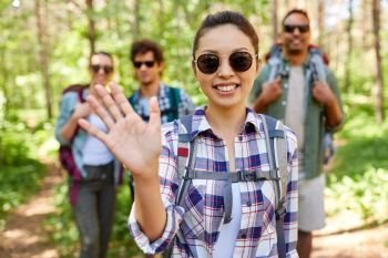 travel, tourism, hike and people concept - group of friends with backpacks and asian woman waving hand in forest. friends with backpacks on hike in forest