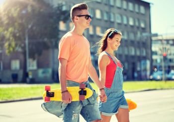 summer holidays, extreme sport and people concept - happy teenage couple with short modern cruiser skateboards walking along city street. teenage couple with skateboards on city street