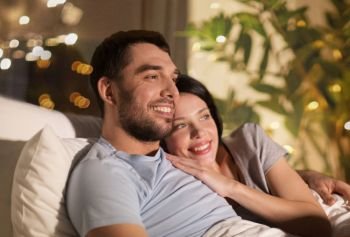 people, family and leisure concept - happy couple watching tv in bed at night at home. happy couple watching tv in bed at night at home