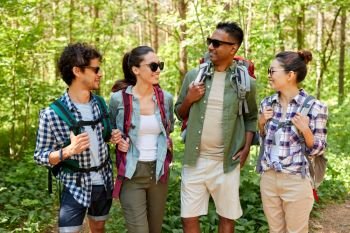 travel, tourism, hike and people concept - group of friends with backpacks talking in forest. friends with backpacks on hike talking in forest