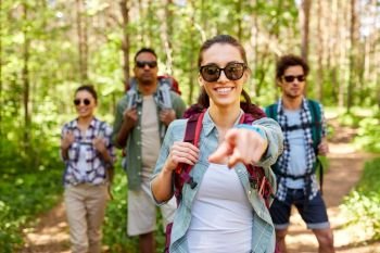 travel, tourism, hike and people concept - group of friends with backpacks and woman pointing finger to you in forest. friends with backpacks on hike in forest