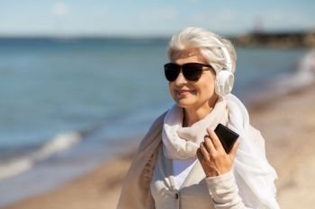 old people and leisure concept - happy smiling senior woman using smartphone on beach in estonia. senior woman using smartphone on beach