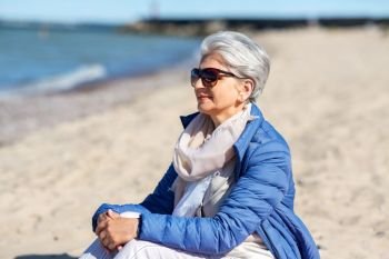 people and leisure concept - happy senior woman in sunglasses and jacket on beach in estonia. happy senior woman in jacket on beach