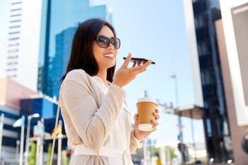 communication, lifestyle and technology concept - happy smiling young asian woman in sunglasses with takeaway coffee cup recording voice message by smartphone on city street. woman recording voice by smartphone in city