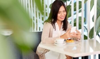 technology and people concept - happy asian woman with smartphone and cake at cafe or coffee shop. asian woman with smartphone at cafe or coffee shop