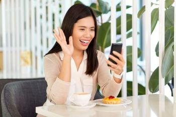 technology, communication and people concept - happy asian woman having video call on smartphone at cafe or coffee shop. woman having video call on smartphone at cafe