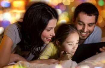 people and family concept - happy mother, father and little daughter with tablet pc computer in bed at night at home. family with tablet pc in bed at night at home