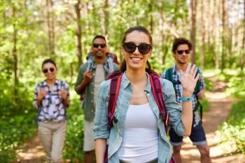 travel, tourism, hike and people concept - group of friends with backpacks and woman waving hand in forest. friends with backpacks on hike in forest