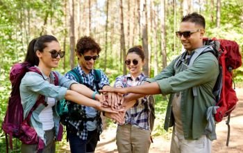 travel, tourism, hike and friendship concept - group of friends with backpacks stacking hands in forest. friends with backpacks stacking hands in forest