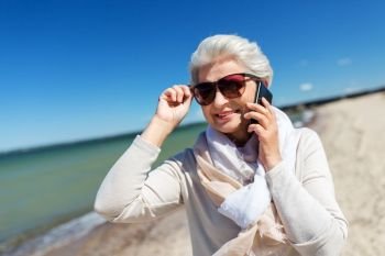 old people and leisure concept - happy smiling senior woman calling on smartphone on beach in estonia. senior woman calling on smartphone on beach