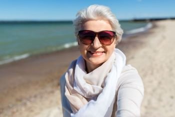 old people and leisure concept - happy smiling senior woman in sunglasses taking selfie on beach in estonia. senior woman in sunglasses taking selfie on beach
