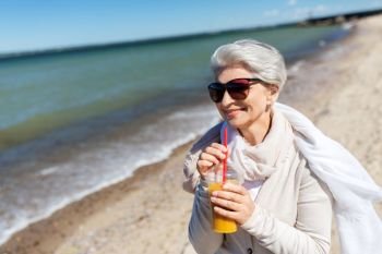 people and leisure concept - senior woman in sunglasses drinking shake, orange juice or smoothie on beach in estonia. senior woman drinking orange juice on beach