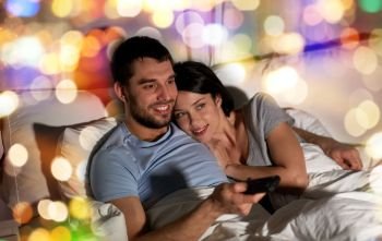 people, family and leisure concept - happy couple watching tv in bed at night at home. happy couple watching tv in bed at night at home