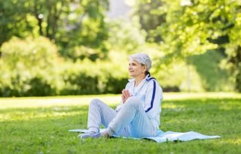 fitness, sport and healthy lifestyle concept - happy smiling senior woman doing yoga on exercise mat at summer park. happy senior woman doing yoga at summer park