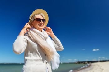 people and leisure concept - portrait of happy senior woman in sunglasses and straw hat on beach in estonia. happy senior woman in sunglasses and hat on beach