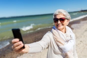 old people and leisure concept - happy smiling senior woman taking selfie by smartphone on beach in estonia. senior woman taking selfie by smartphone on beach