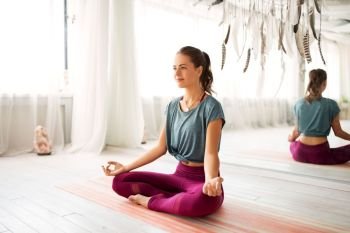 mindfulness, spirituality and healthy lifestyle concept - woman meditating in lotus pose at yoga studio. woman meditating in lotus pose at yoga studio