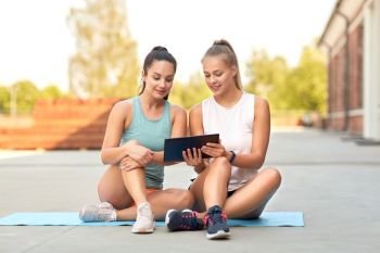 fitness, sport and healthy lifestyle concept - smiling young women or female friends with tablet computer on rooftop. sporty women or friends with tablet pc on rooftop