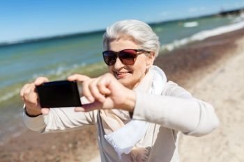 old people and leisure concept - happy smiling senior woman taking selfie by smartphone on beach in estonia. senior woman taking selfie by smartphone on beach