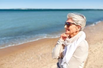 people and leisure concept - portrait of happy senior woman in sunglasses and scarf on beach in estonia. portrait of senior woman in sunglasses on beach
